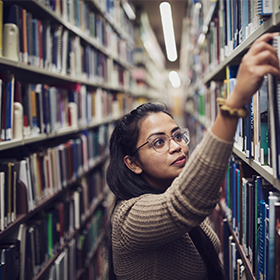 Student selecting a book from the library shelf.